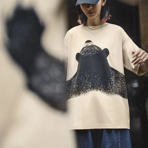 Person wearing a beige t-shirt with a bear graphic design.